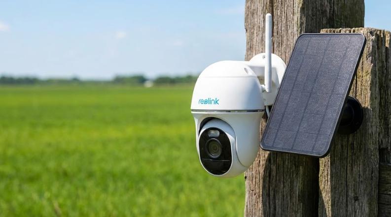 Cámara de vigilancia exterior con panel solar instalada en poste de madera y fondo de campo verde. Opción B (SEO): Cámara de seguridad inalámbrica con carga solar montada en entorno rural sin electricidad.