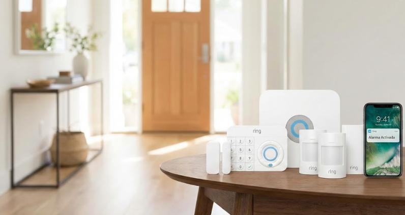 Kit de alarma Ring completo sobre mesa moderna con smartphone mostrando notificación de Alarma Activada. Opción B (Enfocada a SEO): Sistema de seguridad Ring y control móvil con alerta de alarma activada en entorno doméstico.