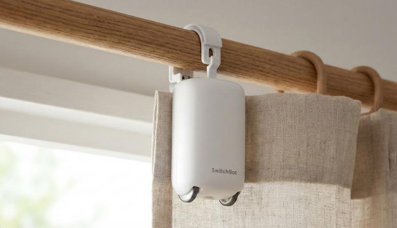 Primer plano de un robot SwitchBot Curtain blanco instalado en una barra de cortina de madera para automatizar la apertura.